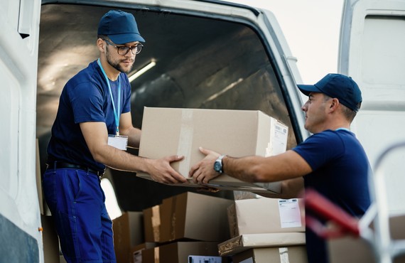 Delivery men loading carboard boxes in a van while getting ready for the shipment.